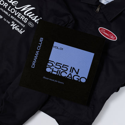 A black jacket with white printed graphics and a red oval 'Drama Club' patch, laid flat with a black vinyl cover featuring a blue panel and the text '5:55 IN CHICAGO Vol.01' and 'Drama Club'